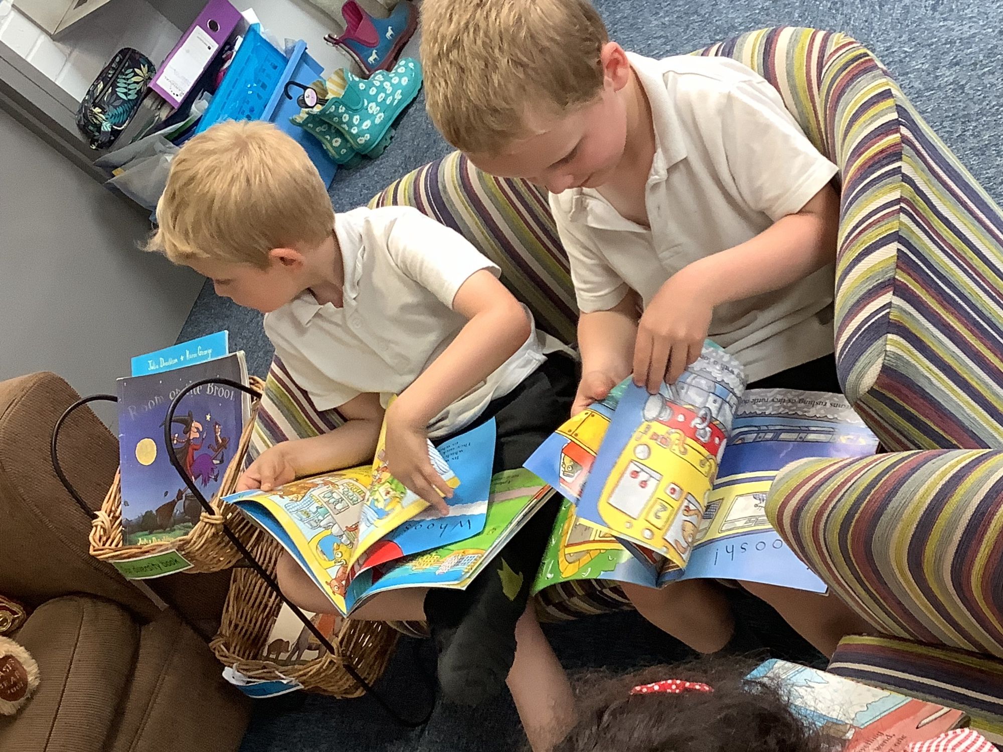 Two children sitting on a stripy sofa reading.