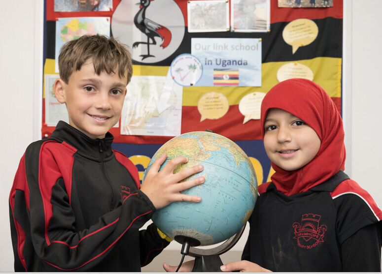 Two children either side of a globe in front of a display about the Ugandan link school.