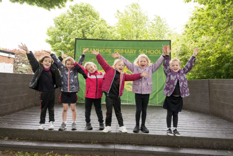 Five children shouting 'Ta-Da!' with arms raised on the playground stage.