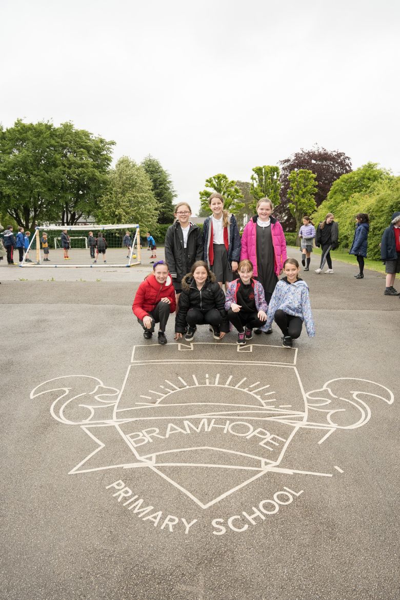 Children standing behind painted crest on playground floor.