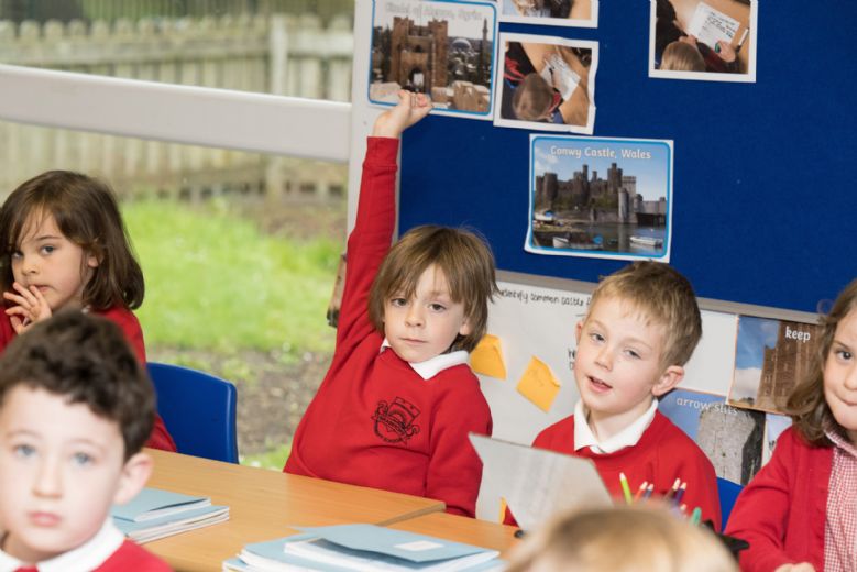 Child with hand up in classroom.