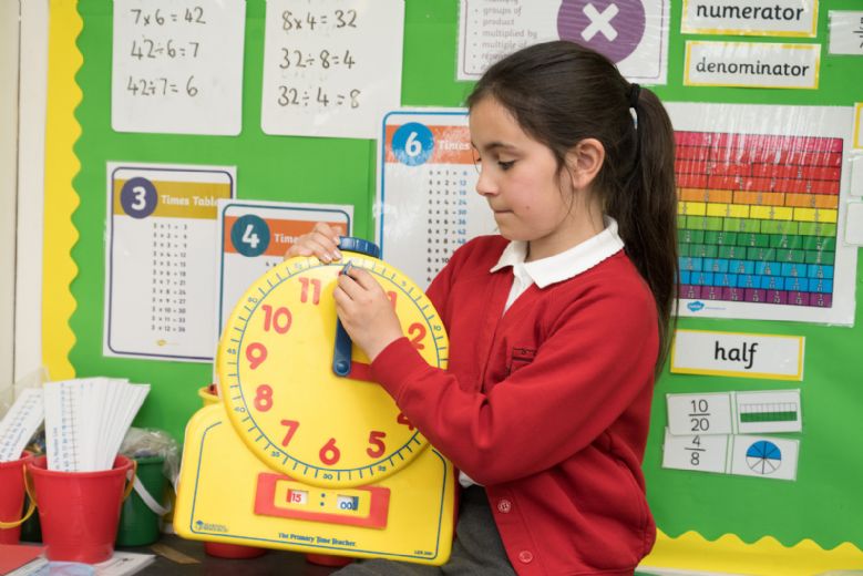 Child sitting changing time on large plastic clock.