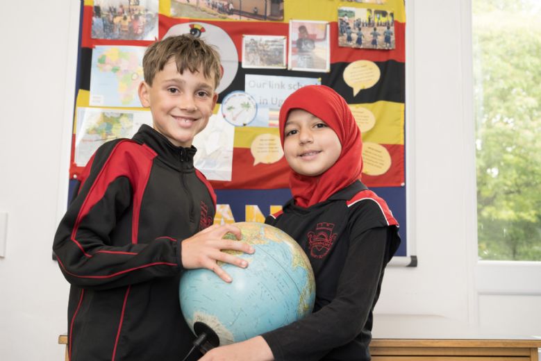 Two children holding a globe in front of a display about Ugandan link school.