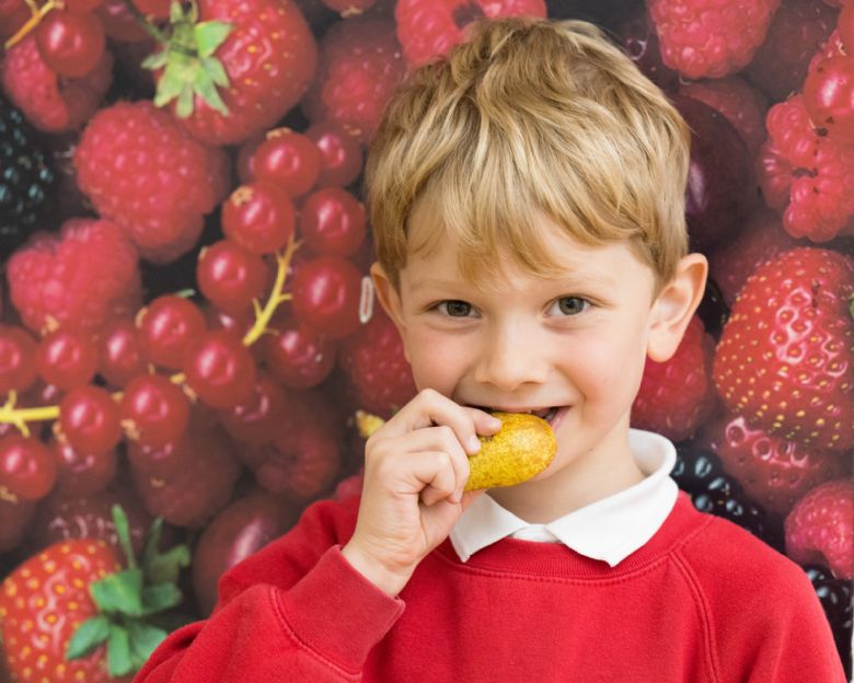 Child biting a pear in front of a large photo of edible red berries.