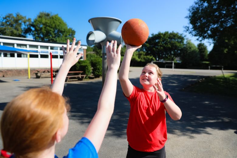 Two children playing netball in the sun,