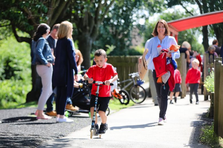 Parent following child on scooter into school.