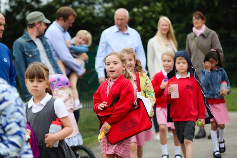 Children walking into school with parents in the background.